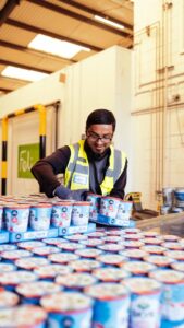 Worker handling trays of surplus yoghurt products at a food redistribution warehouse.